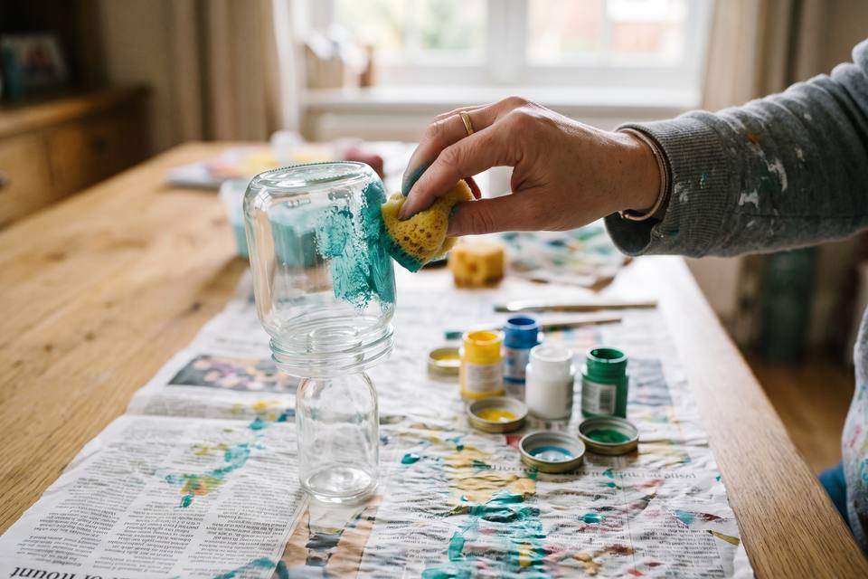 Une main tamponne de la peinture turquoise à l'éponge sur un bocal retourné