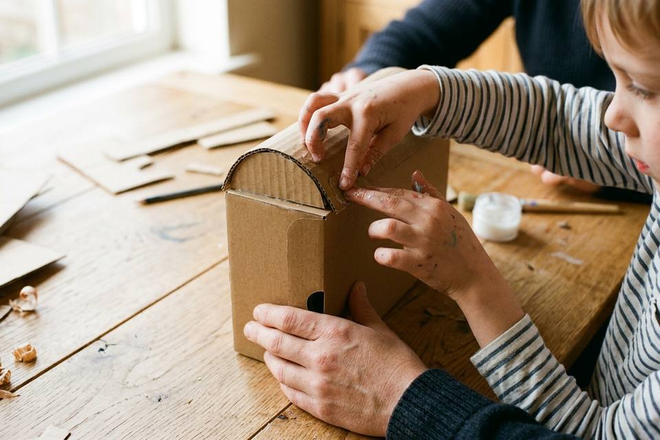 Deux mains d'enfant collent une bande de carton cintrée sur le haut de la boîte pour former le toit
