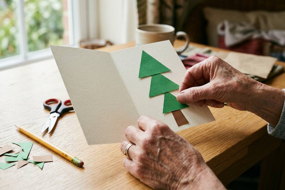 Des mains posent les triangles verts du sapin sur la carte pliée, avant le collage