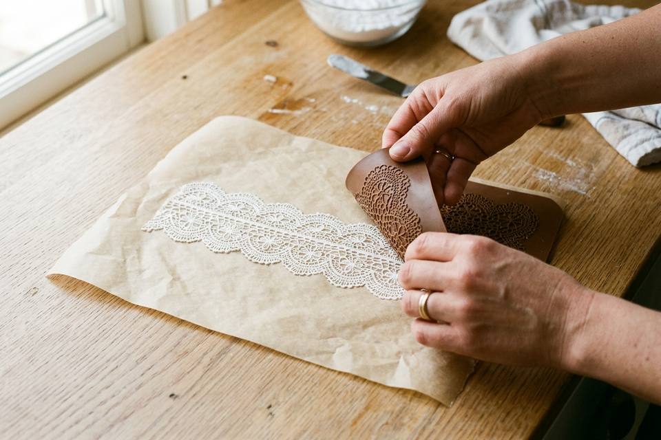 Des mains retournent le tapis en silicone pour décoller une bande de dentelle de sucre sur du papier cuisson