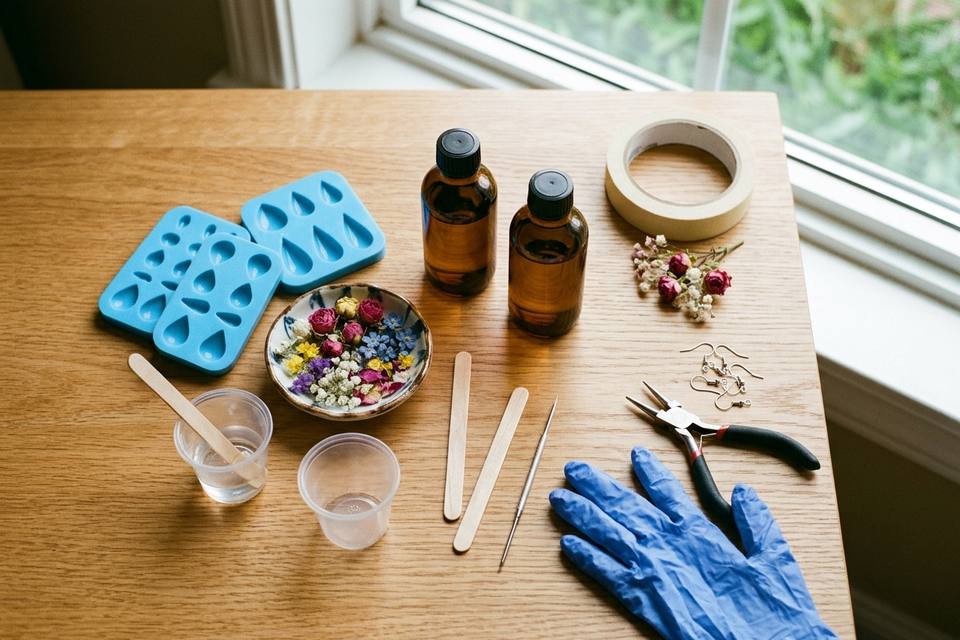 Le matériel à plat : résine époxy en deux flacons, moules en silicone, fleurs séchées, gobelets, pique, gants et crochets de boucles d'oreilles