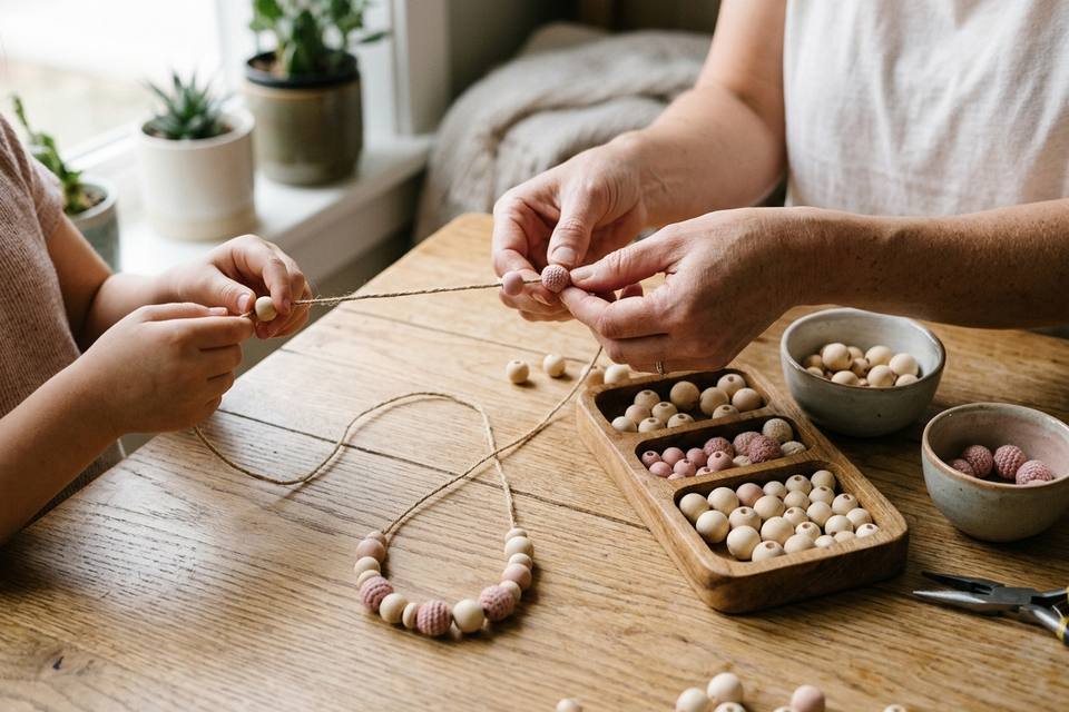 Deux mains font glisser des perles en bois et en coton rose sur le fil, depuis la planchette