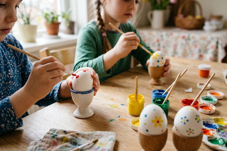 Des mains d'enfant peignent des pois et des fleurs sur des œufs posés dans des coquetiers